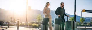 NOMATIC Check-In Luggage collection banner, two people standing outdoors with green check-in luggage at sunset