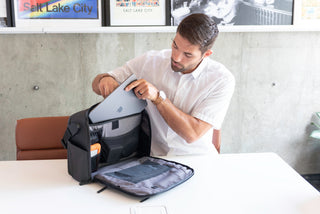 NOMATIC Laptop Bags collection banner, man placing a laptop into an open laptop bag with organized compartments