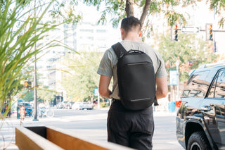 NOMATIC Slings & Hip Packs collection banner, man walking down a city sidewalk wearing a black sling backpack