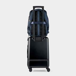 Black suitcase with a blue backpack on top against a light gray background